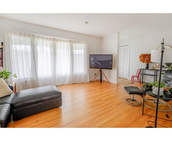 A living room with a black leather sofa and a television on a tripod.