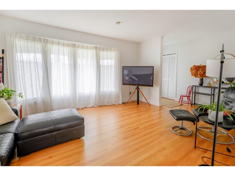 A living room with a black leather sofa and a television on a tripod.
