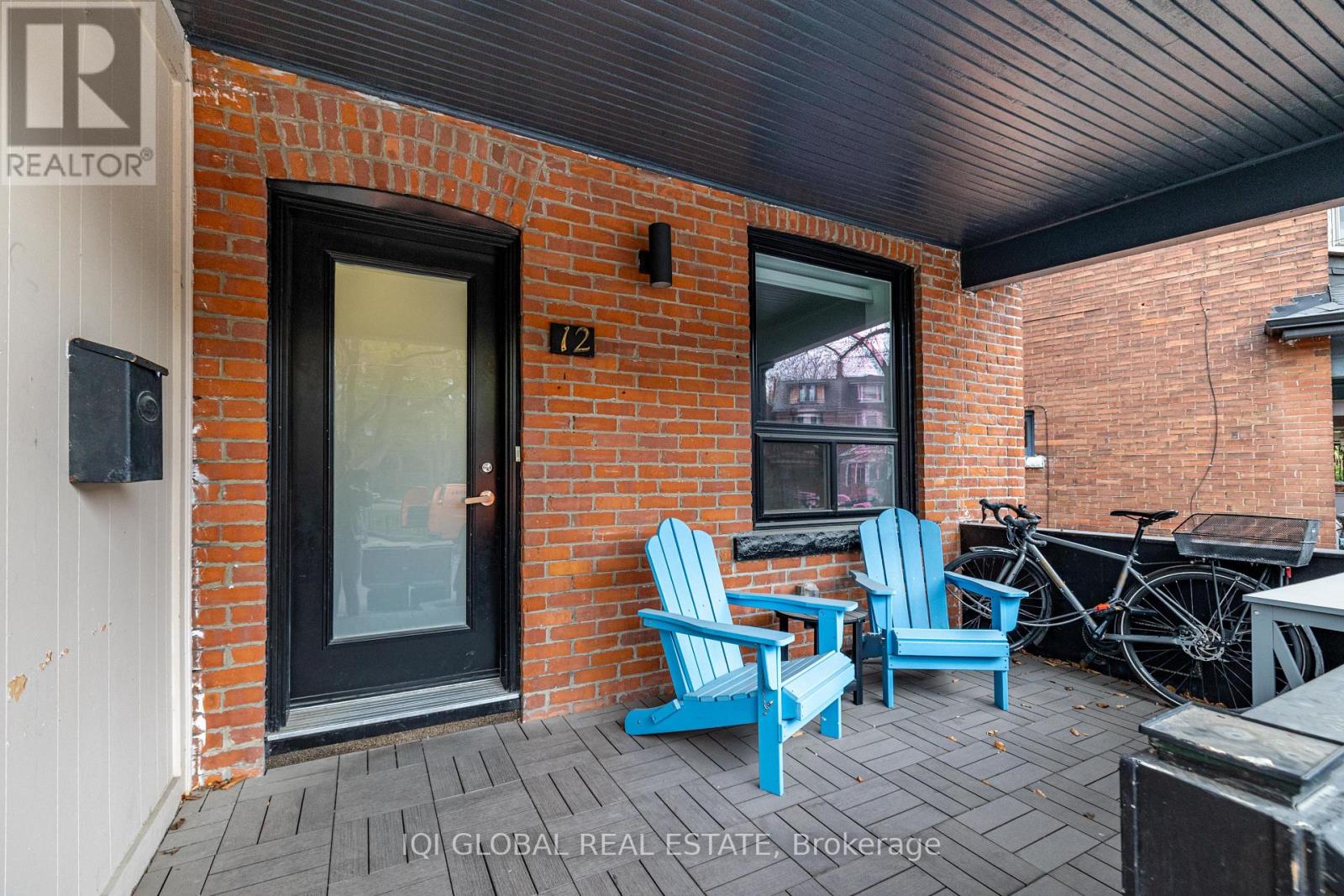 A patio with a black door, a window, and two blue chairs.