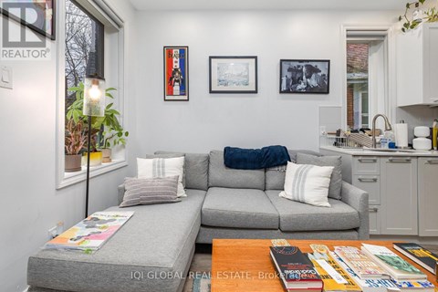A living room with a grey couch, a coffee table with magazines and a book, and a kitchen area in the background.