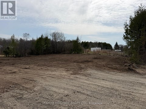 A dirt field with trees and a building in the distance.