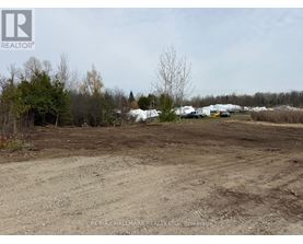 A dirt field with a few trees and buildings in the distance.