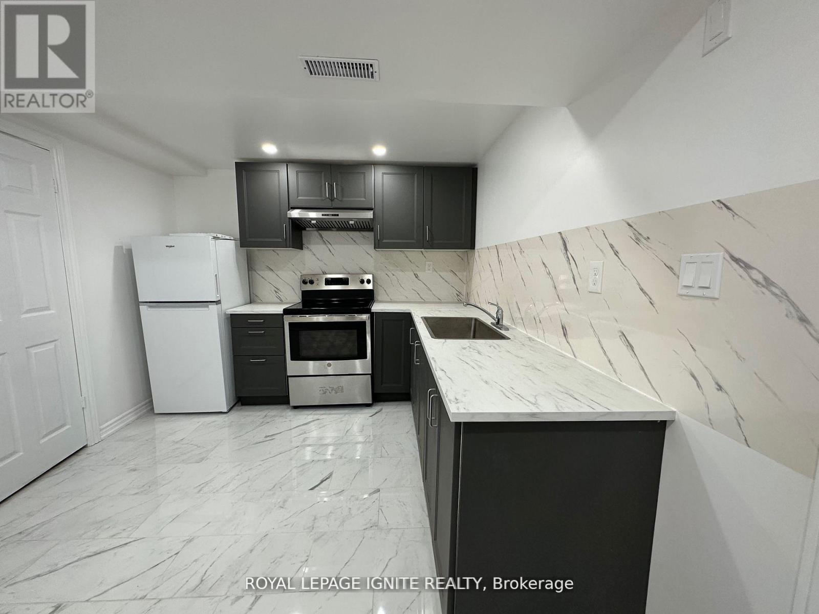 A kitchen with a white fridge, black cabinets, and a marble countertop.