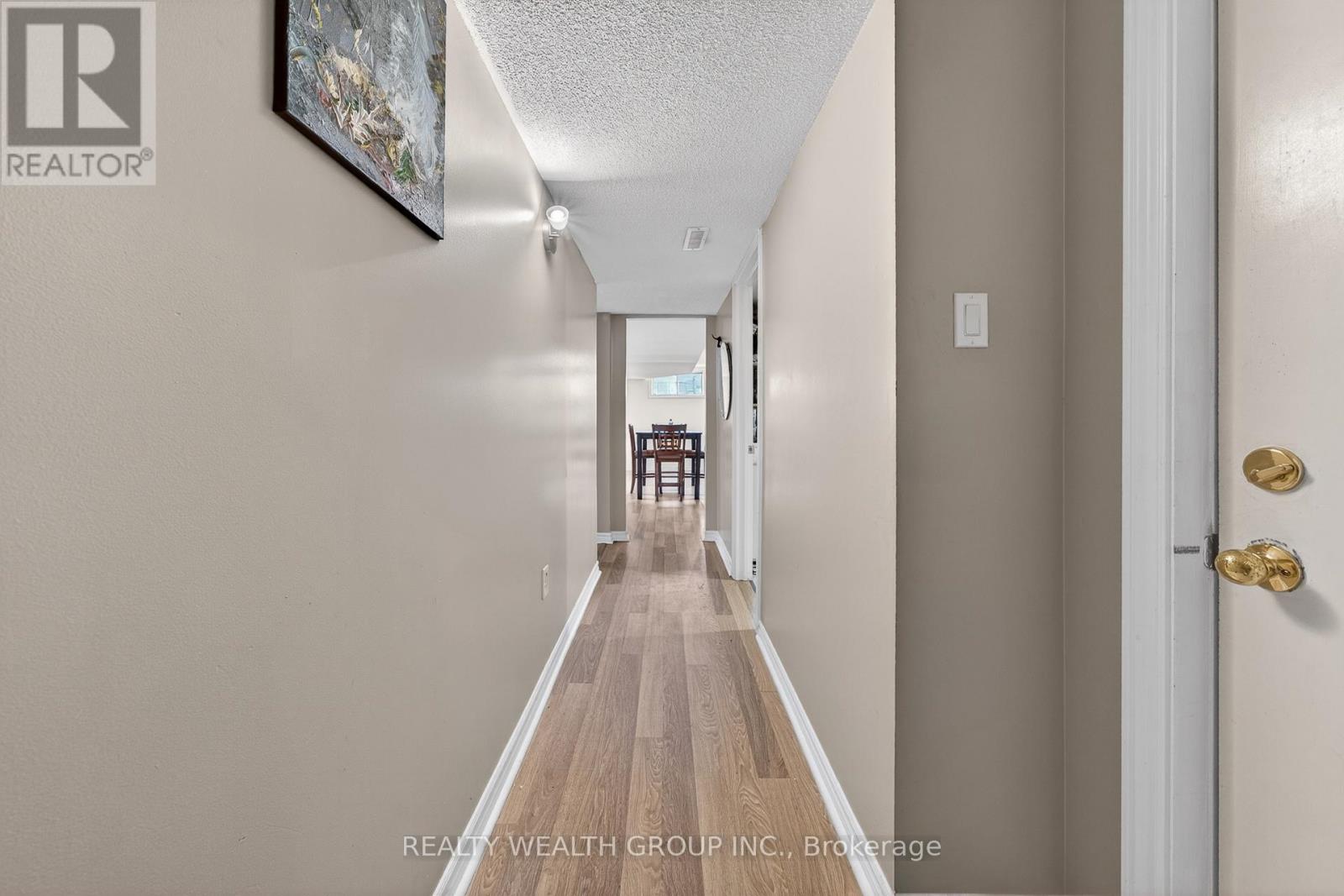 A hallway with a wooden floor and white walls leading to a door.