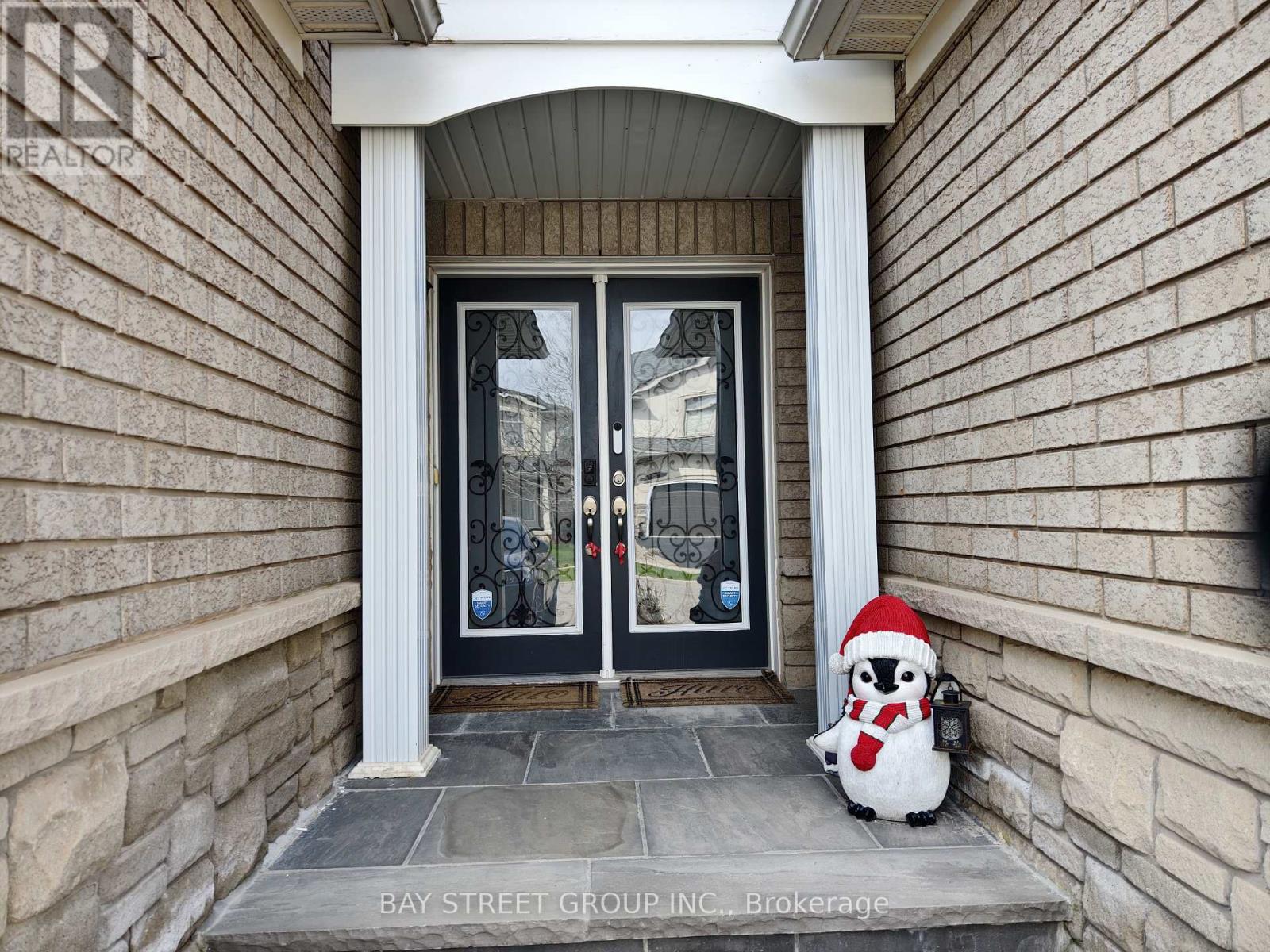 A penguin toy wearing a Santa hat sits on the steps of a house.