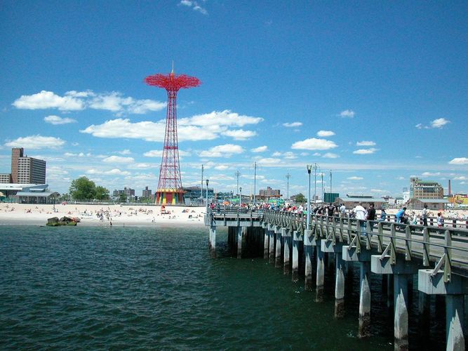A pier with people walking on it and a red tower in the background.