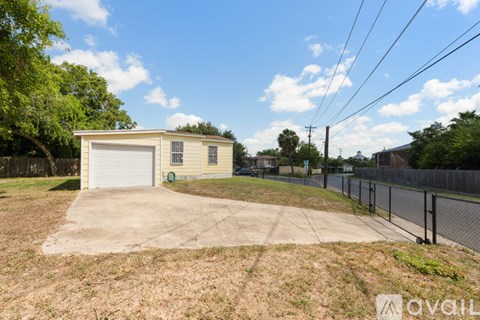 A small garage with a white door is surrounded by a fence and trees.
