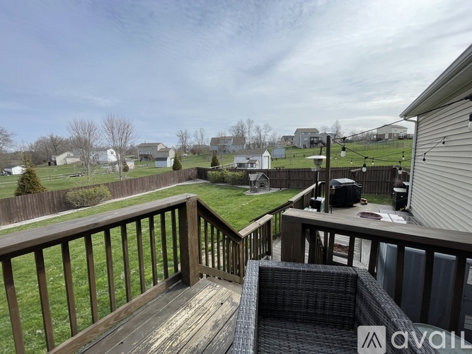 A deck with a wicker chair and a wooden railing overlooks a grassy area.