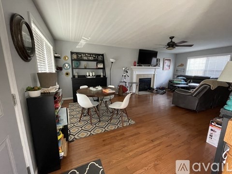 A living room with a black refrigerator, a white dining table with four chairs, a fireplace, and a television on the wall.