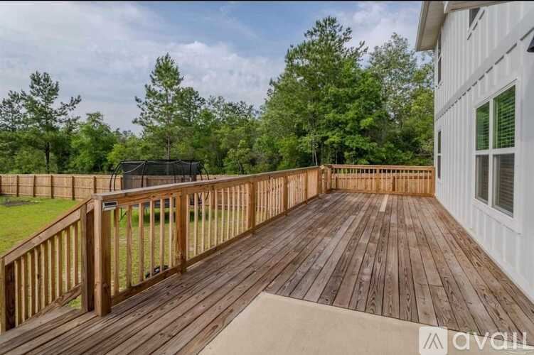 A wooden deck with a white house and trees in the background.