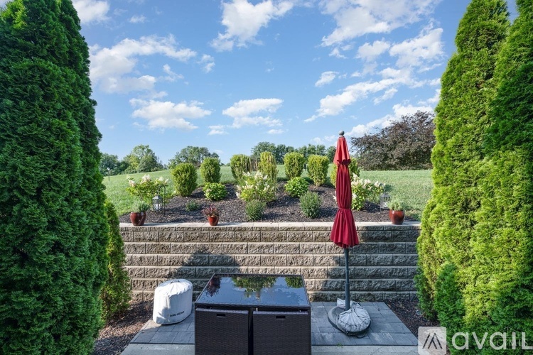 A red umbrella stands on a patio with a stone wall and a hot tub in the background.
