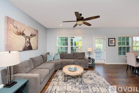 A living room with a grey couch, a coffee table, a painting of a deer head and a ceiling fan.
