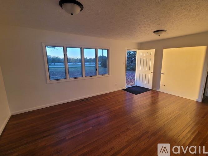 A room with wooden floors and a large window overlooking a field.