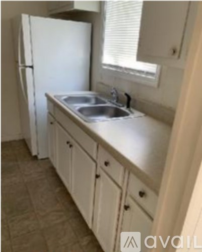 A kitchen with a white fridge, sink and cabinets.