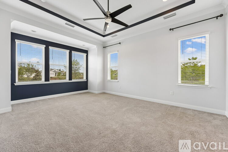 A spacious room with a carpeted floor, a ceiling fan, and large windows.