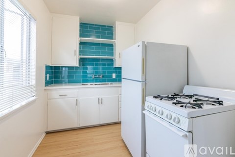 A kitchen with a white stove and white cabinets with blue backsplash.