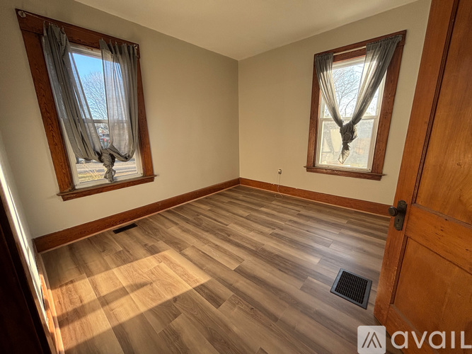 A room with wooden flooring and two windows with curtains.