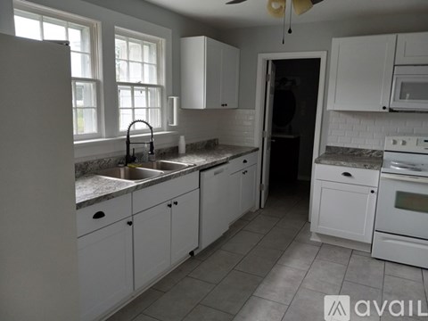 A kitchen with white cabinets and appliances, a window, and a fan.