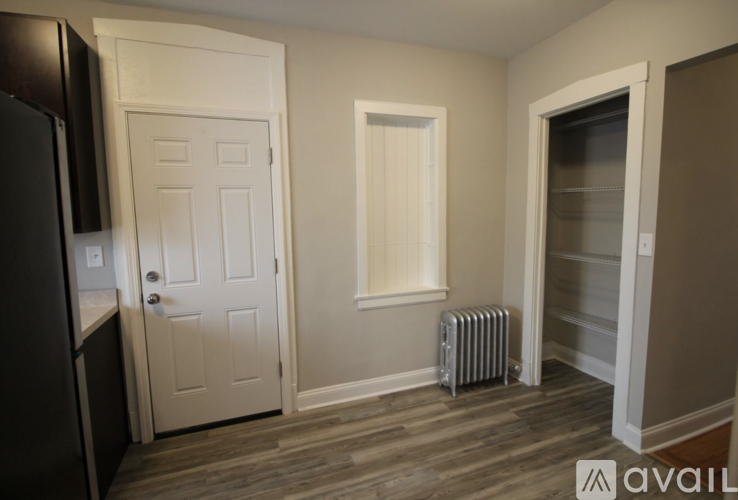A room with a white door, a window with blinds, and a radiator on the floor.