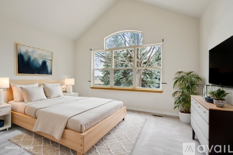 A bedroom with a large bed, a painting on the wall, and a window with a view of trees.