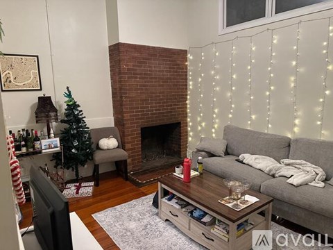 A living room with a grey couch, a coffee table, a fireplace, and a Christmas tree.