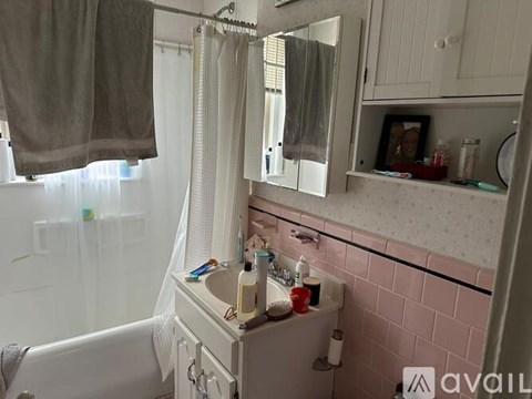A bathroom with a white tub, pink tiles, and a white vanity with a mirror.