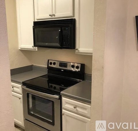 A black microwave is mounted above a stove in a kitchen.