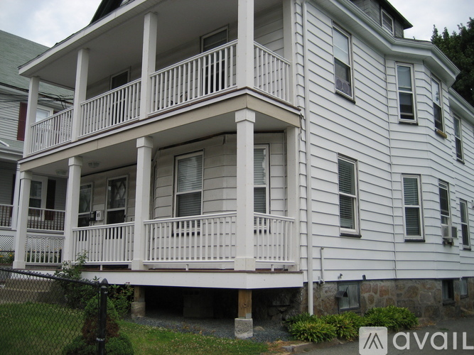 A white two-story house with a balcony and a fence.