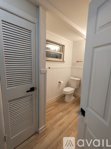 A white toilet sits in a small bathroom with a wooden floor and white walls.