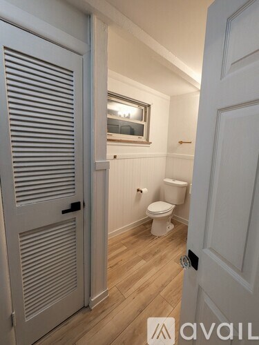 A white toilet sits in a small bathroom with a wooden floor and white walls.