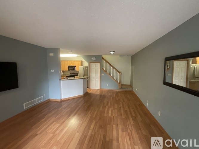 A spacious living room with wooden flooring and a staircase leading to the upper level.