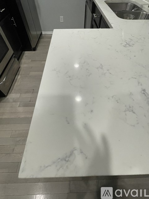 A white marble countertop in a kitchen with a sink and stainless steel appliances.