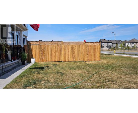 A wooden fence in a yard with a house and other houses in the background.
