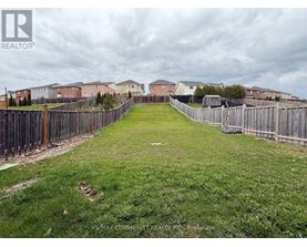 A grassy yard with a fence and houses in the background.