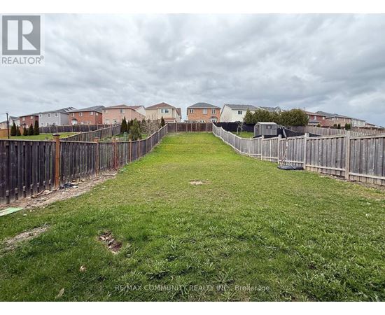 A grassy yard with a fence and houses in the background.