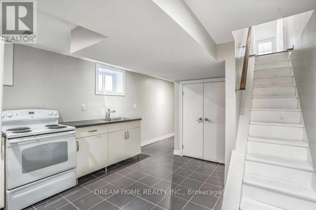 A white kitchen with a stove top oven and a staircase.