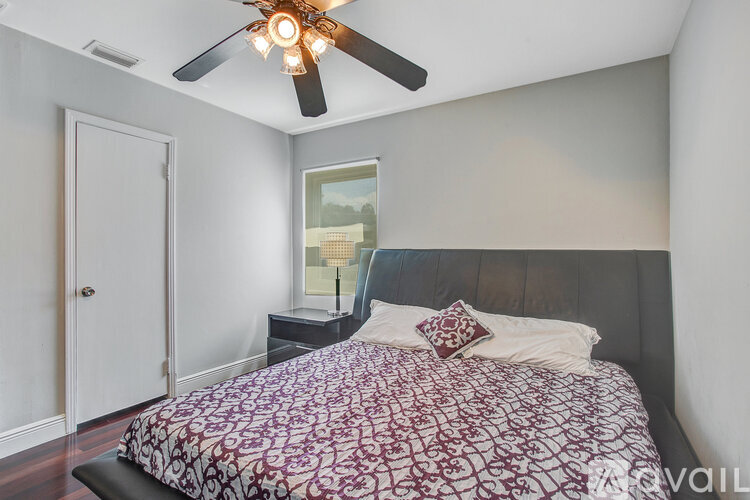 A bedroom with a bed, a ceiling fan, and a painting on the wall.