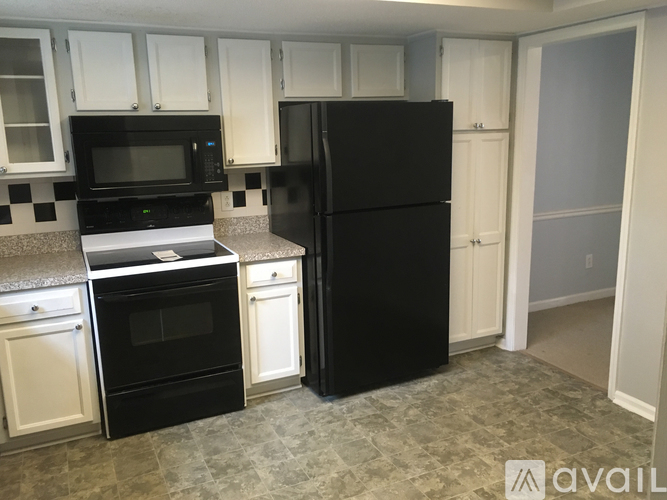 A black refrigerator stands in a kitchen with white cabinets and a black and white checkered backsplash.