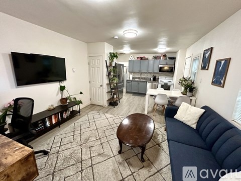 A living room with a black couch, a wooden coffee table, and a television on the wall.