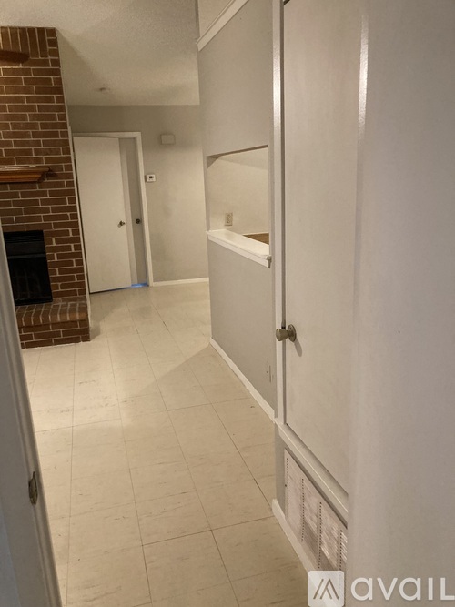 A white door with a gold handle is in a white hallway.