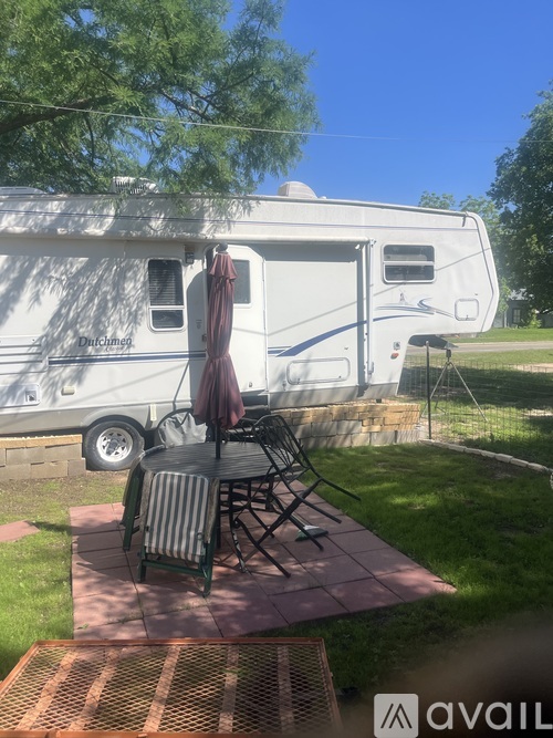 A white RV is parked in a yard with a table and chairs set up outside.
