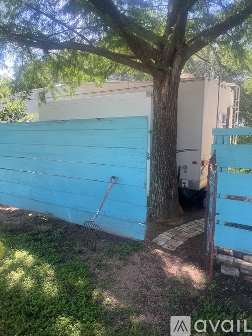 A tree is in front of a blue fence and a white building.