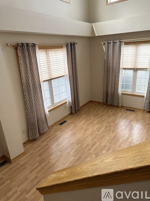 A room with wooden flooring and two windows with curtains.