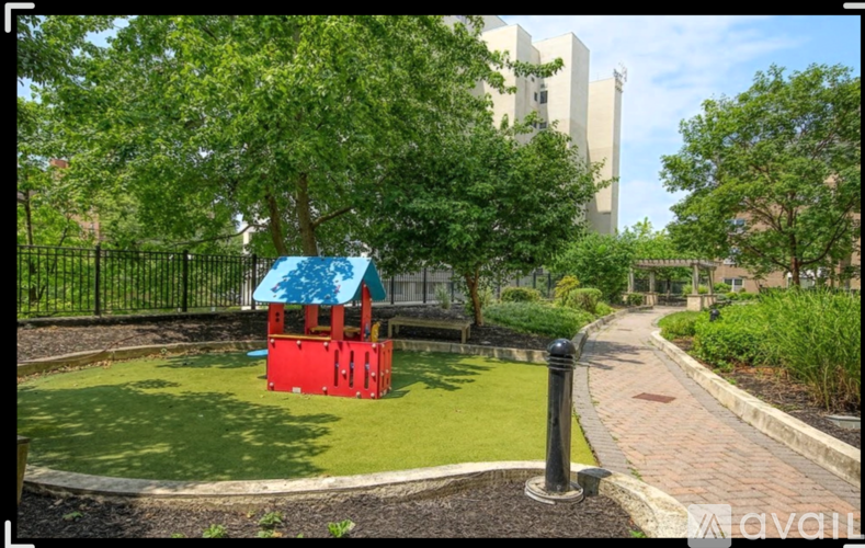 A playground with a red slide and a blue roof is surrounded by a fence and a brick path.