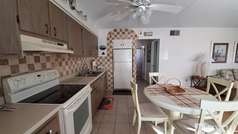 A kitchen with a white oven and microwave, a white fridge, and a white dining table with chairs.