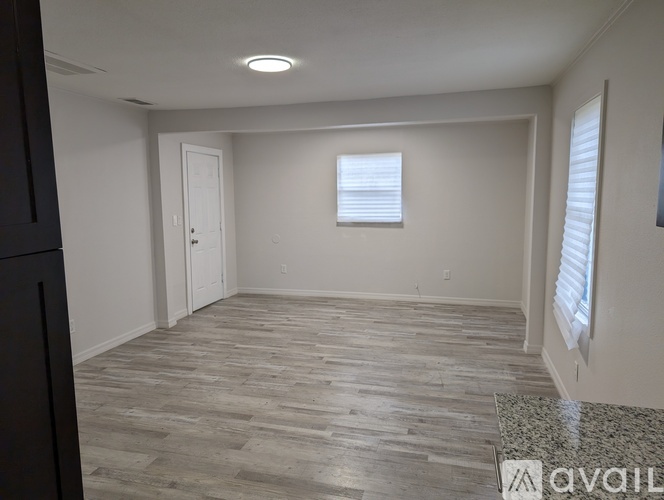 A spacious room with wooden flooring and a window with blinds.