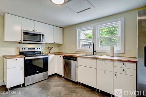 A kitchen with white cabinets and appliances, a window, and a tiled floor.