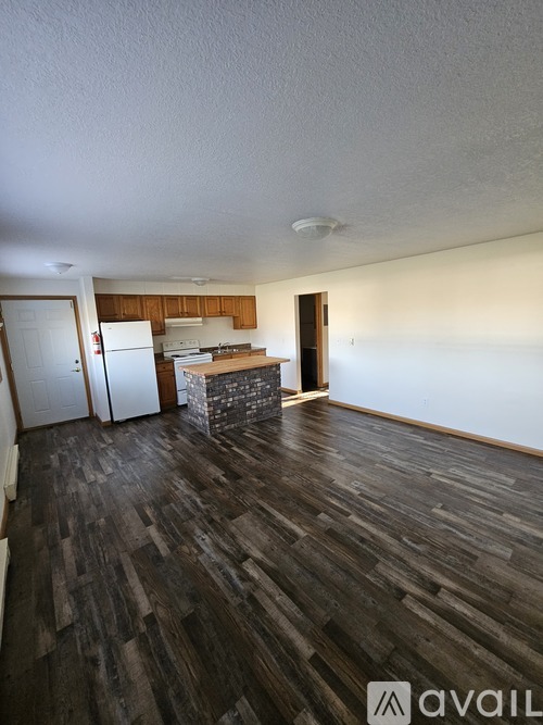 A room with wooden flooring and a kitchen area in the background.