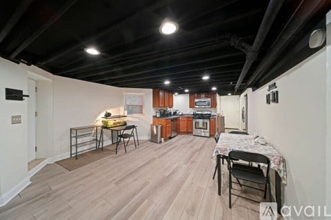 A room with a dining table and chairs in the foreground and a kitchen in the background.