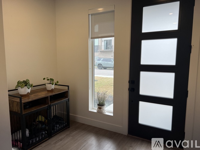 A black door with a glass panel is open to a view of a car and a building outside.